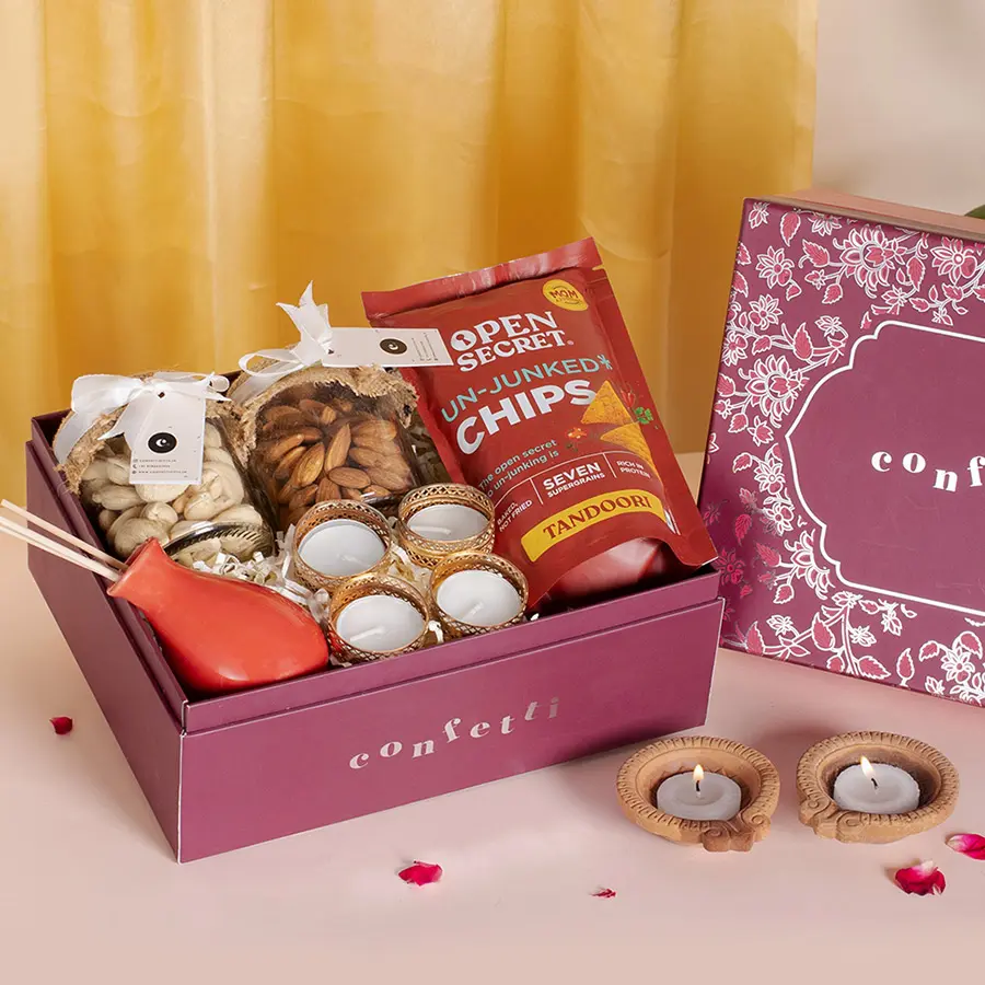 Red Botanical Diwali Delights Box with almonds, cashews, tea light candles, reed diffuser, and Tandoori chips in an elegant red packaging