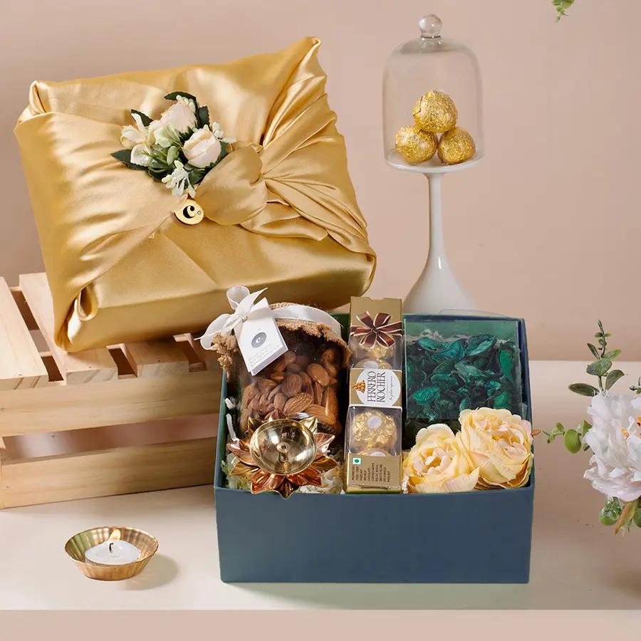 Diwalis Finest Gift Selection featuring a glass jar of almonds, Ferrero chocolates, a brass diya, green potpourri, and an elegant Diwali lantern box, all beautifully packaged in satin.