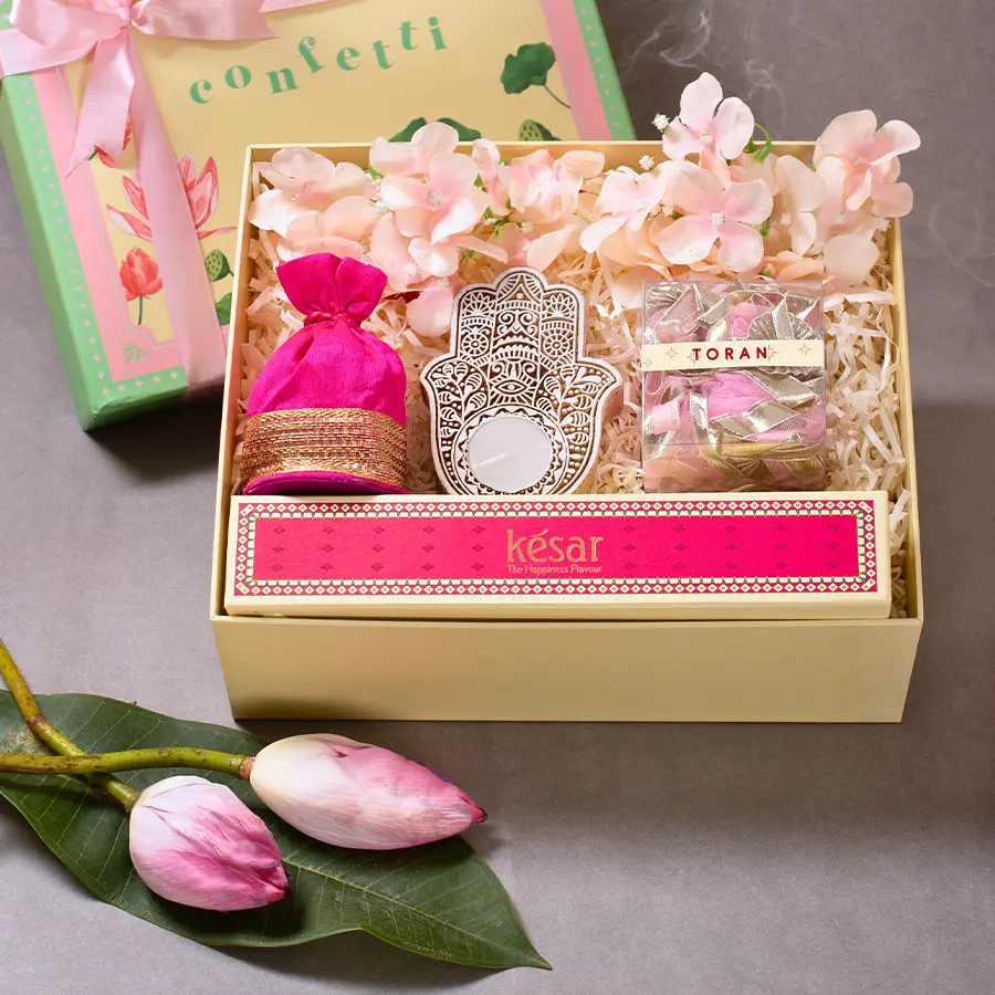 Diwali Celebration Essentials Box featuring Pink Torans, a handcrafted wooden candle, Kesar sweets, a Pink Potli of dry fruits, flower decor, all in an elegant Green Lotus Box.