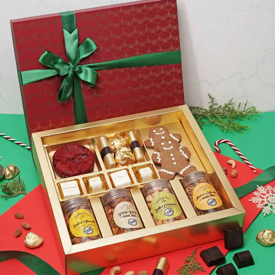 Christmas Gourmet Delights Variety Box showcasing a selection of festive treats including Red Velvet Cookies, Strawberry Chocolate Logs, Almond Chocolate Rocks, Gingerbread Men, and various savory snacks like Salted Almonds and Trail Mixes.
