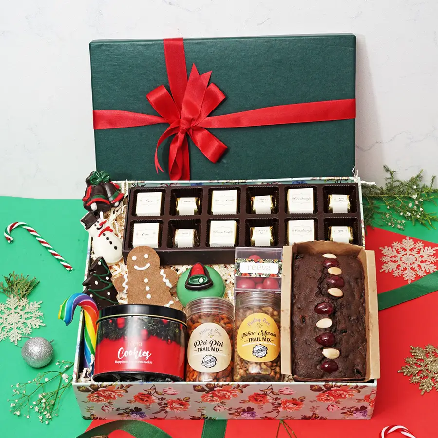 Chocoholics Delight Assorted Treasures Box featuring assorted chocolates, a chocolate snowman, Christmas lollipops, a gingerbread cookie, a hot chocolate bomb, trail mixes, cranberry dragees, plum cake, assorted cookies, and a candy cane in a festive presentation.