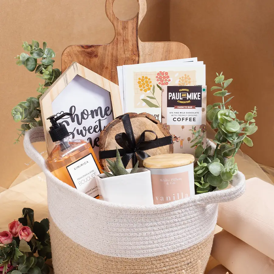 Functional gift hamper featuring a mango wood cheese board, a 2024 calendar, a vanilla scented candle, a home sweet home key holder, wooden coasters, a succulent in a ceramic planter, a planter bag, Kimrica hand soap, and Paul And Mike coffee chocolate.