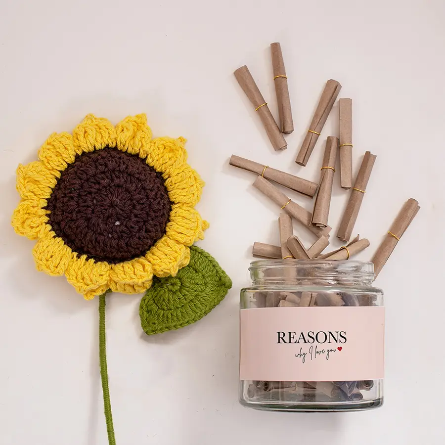 A beautifully arranged gift box filled with a jar of 52 heartfelt love notes, a crochet sunflower, and love-themed wrapping paper, all showcasing a thoughtful surprise for a special someone.