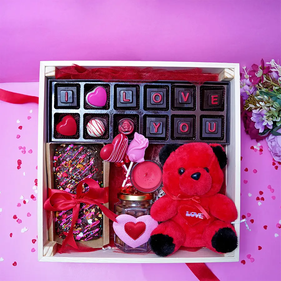 Deluxe Choco Treats Gift Hamper featuring assorted chocolates, heart and rose-shaped lollipops, Hazelnut Nutella tea cake, coated raisins, a scented candle, and a teddy bear.