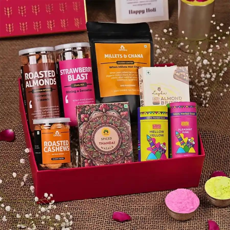Classic Holi Treats Gift Box with gold-foil packaging containing Strawberry Blast Trail Mix, roasted almonds and cashews, Loyka Almond Brittle, Gulab’s Instant Thandai, Herbal Gulaal, and a Holi greeting card