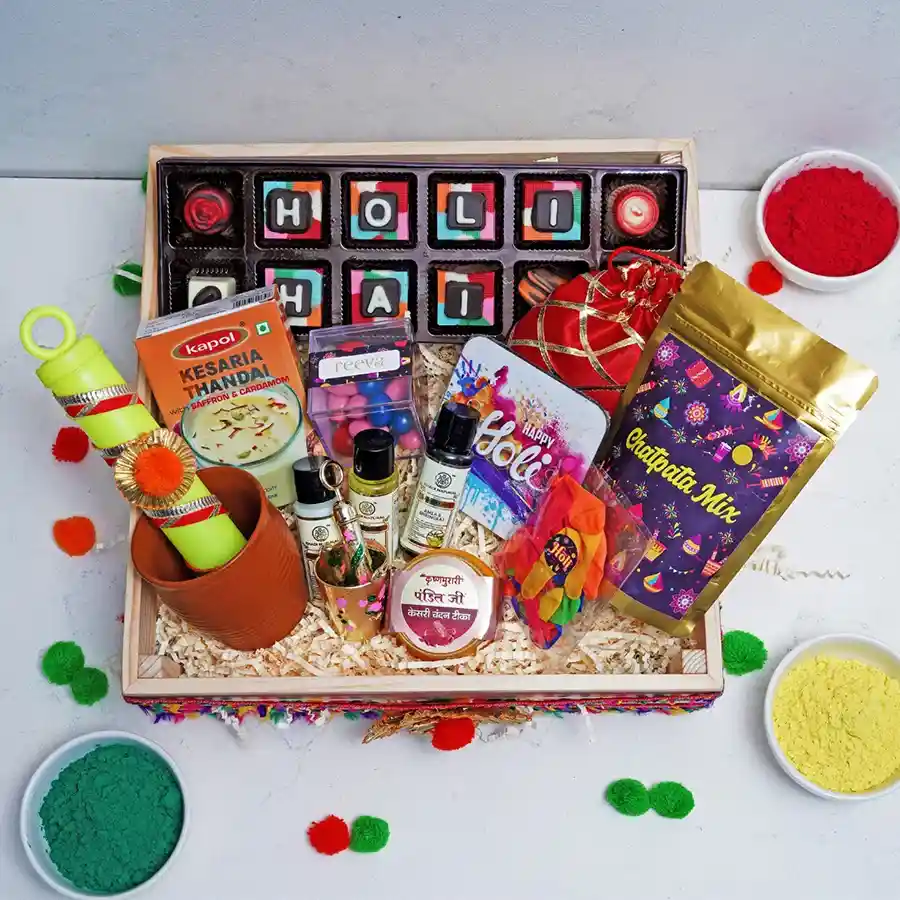 Holi Joy Gift Set featuring chocolate box, Kesaria Thandai, assorted dragees, kullad cup, strawberry logs, Chatpata Mix, Khadi herbal face wash, hair care products, colorful Pichkaris, and festive balloons.