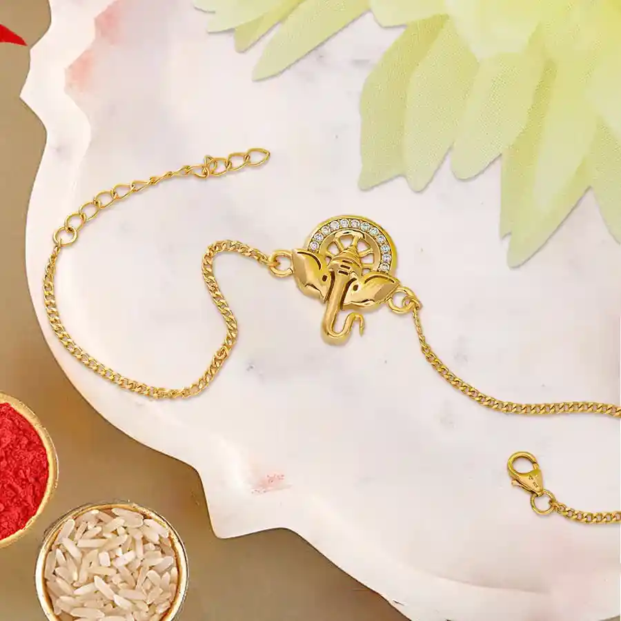 Elegant gold plated rakhi with intricate design, accompanied by roli, tilak, and chawal.