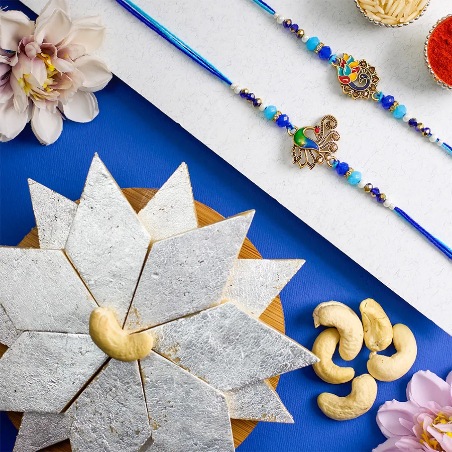 Kundan Rakhi set with two peacock-themed rakhis, Kaju Katli, Roli, Tika, Chawal, and a message card on a decorative background