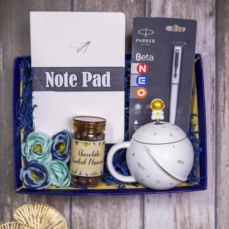 Space Odyssey Gift Box featuring chocolate-coated almonds, a white notepad, a Parker Beta pen, a space-themed coffee mug, and a reusable designer tray.