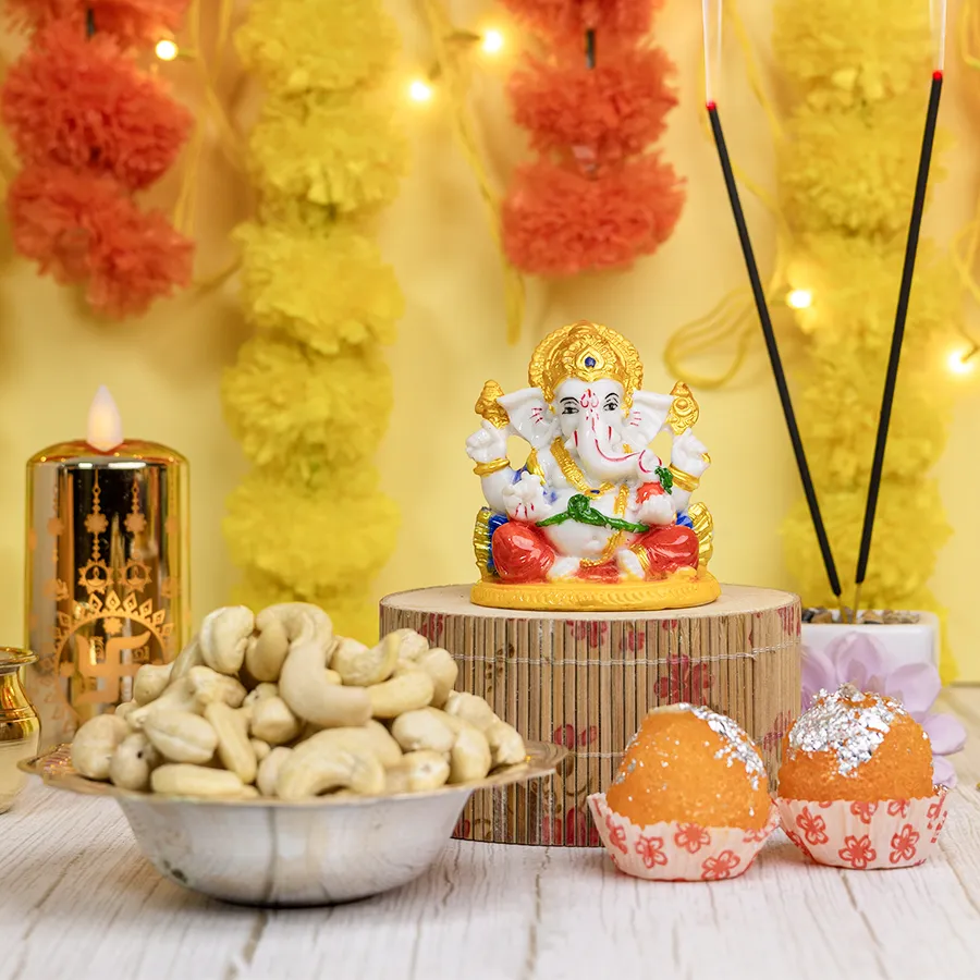 Diwali Blessings N Treats Ensemble featuring a Marble Abhaya Mudra Ganesha, a 100g pack of cashews, laddu candles, and a silver-plated bowl arranged in a reusable basket.