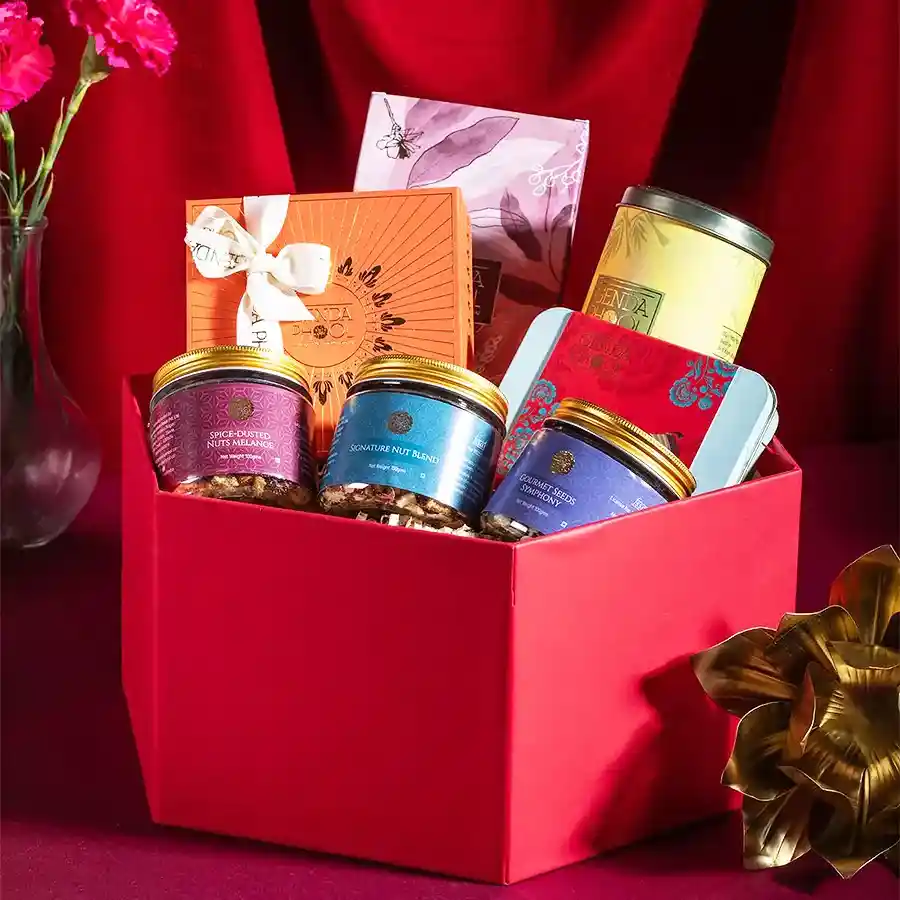 Indulgent Treats Gift Hamper filled with assorted snacks including stuffed Medjool dates, peri peri matthi, pistachio cranberry brittle, mithai bites, nut melange, gourmet seeds, and signature nut blend.