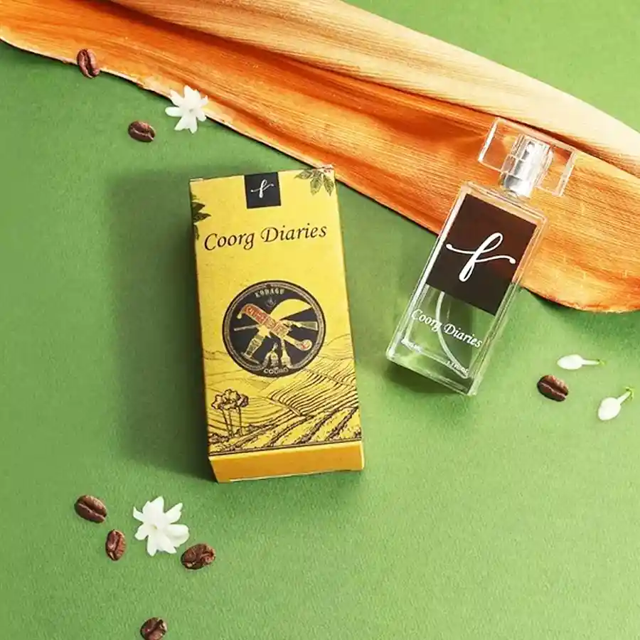 Bottle of Coorg Diaries Coffee Bliss Escape perfume surrounded by coffee beans and lush green foliage