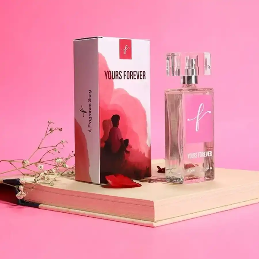 A bottle of First Love Essence Forever Yours perfume surrounded by blooming flowers