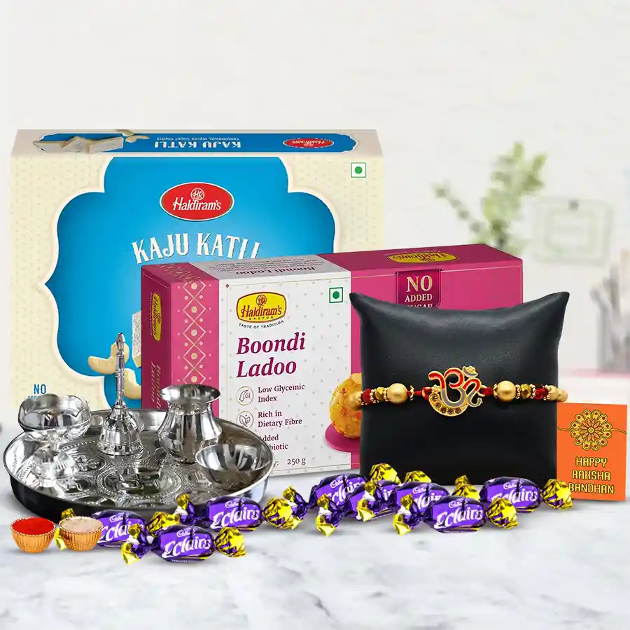 Pious Om Rakhi gift set featuring traditional Om Rakhi, silver-plated Puja Thali, Haldiram Kaju Katli, Boondi Laddoo, Cadbury Eclairs chocolates, Rakhi greeting card, and Roli Chawal Tika.