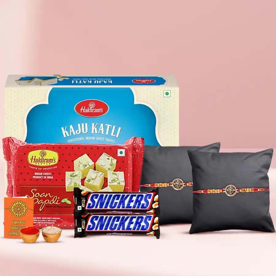 Divine Swastik Rakhi gift pack featuring two Swastik Rakhis, Haldiram's Kaju Katli and Soan Papdi, imported Snickers bars, a Rakhi card, Roli Tilak, and chawal.