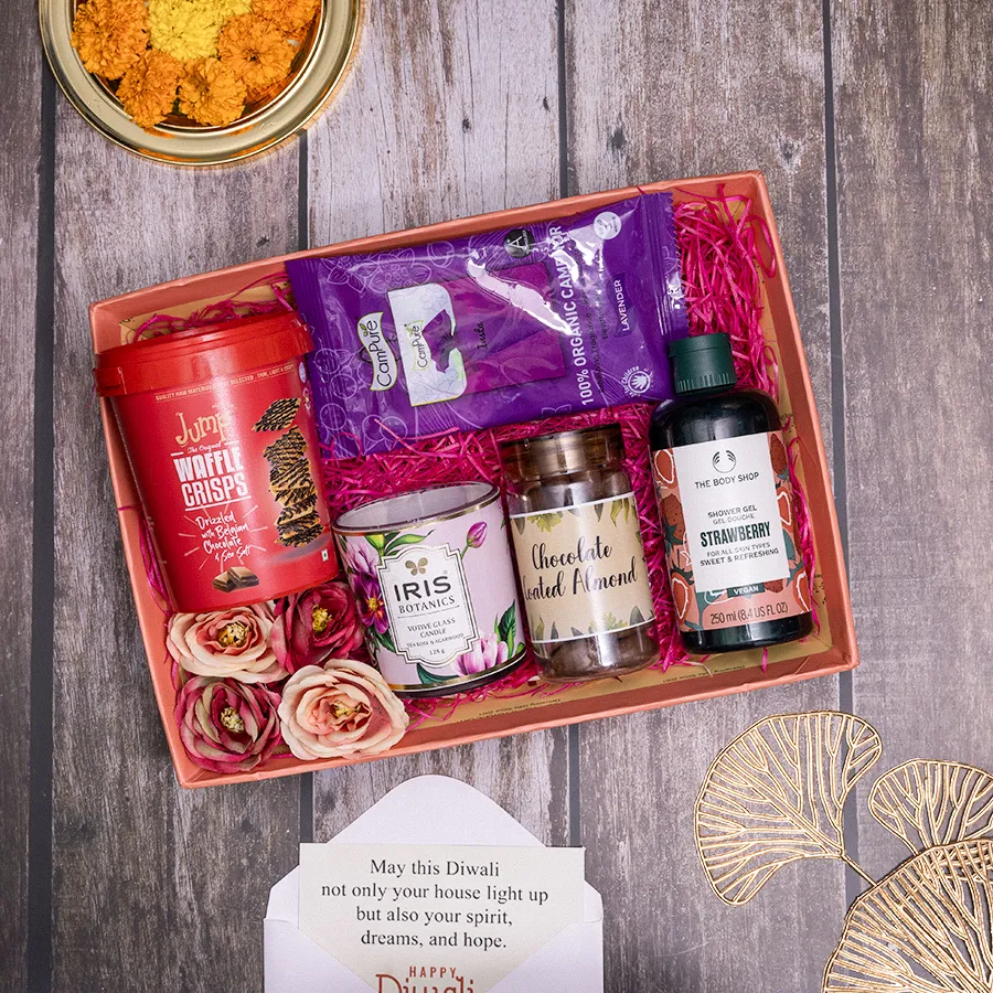 A beautifully arranged hamper filled with gourmet treats including waffle crisps, chocolate-coated almonds, shower gel, room freshener, and a votive candle, all in a reusable basket.