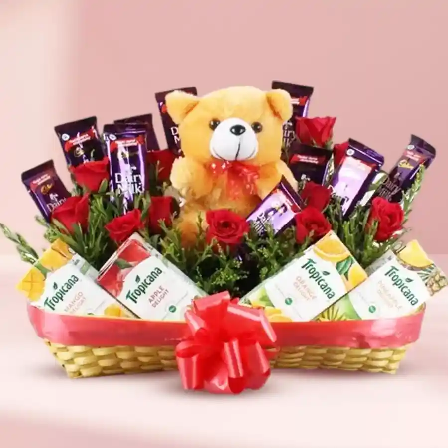 A joyful gift basket featuring Cadbury chocolates, Tropicana juice, a teddy bear, velvet red roses, and confetti.