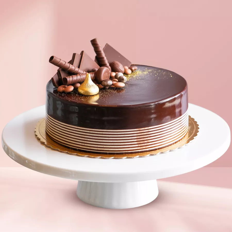 A decadent eggless chocolate cake topped with KitKat bars and chocolate thins, garnished with white cream frosting and chocolate drizzle.