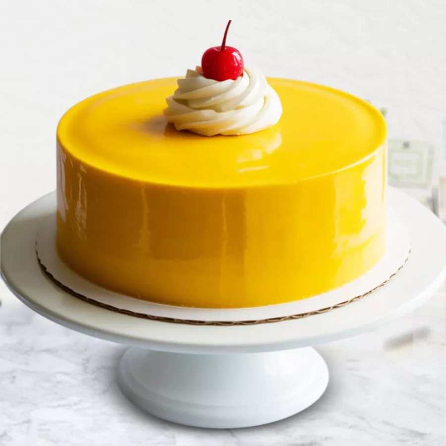 A round Eggless Mango Cake topped with mango syrup and chocolate thins, set on a decorative plate, showcasing its rich flavors and delightful garnishing.