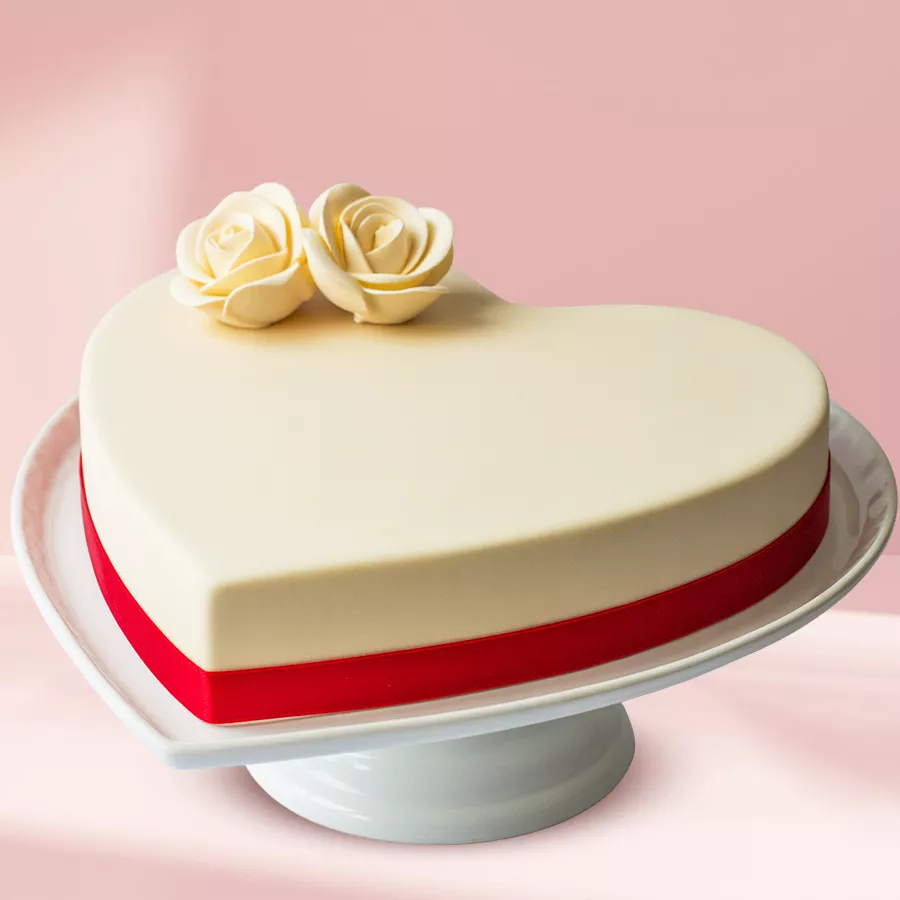 Irresistible Heart Shape Vanilla Fondant Cake with cream roses and a red ribbon, ideal for romantic celebrations.