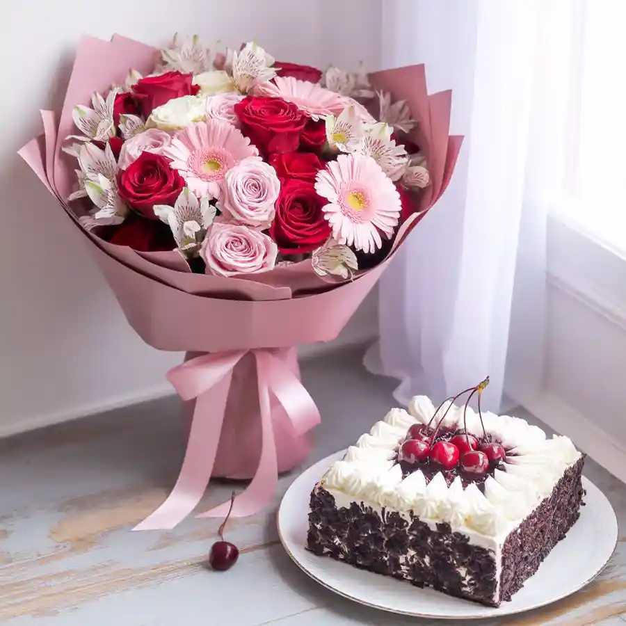 Black Forest Cake with cream and cherries alongside a bouquet of seasonal Gerberas and Carnations.