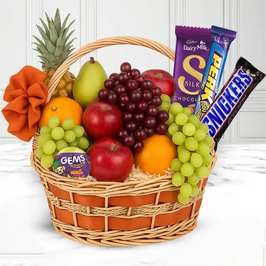 A vibrant basket filled with fresh fruits and assorted chocolates including Cadburys and Snickers, perfect for gifting.