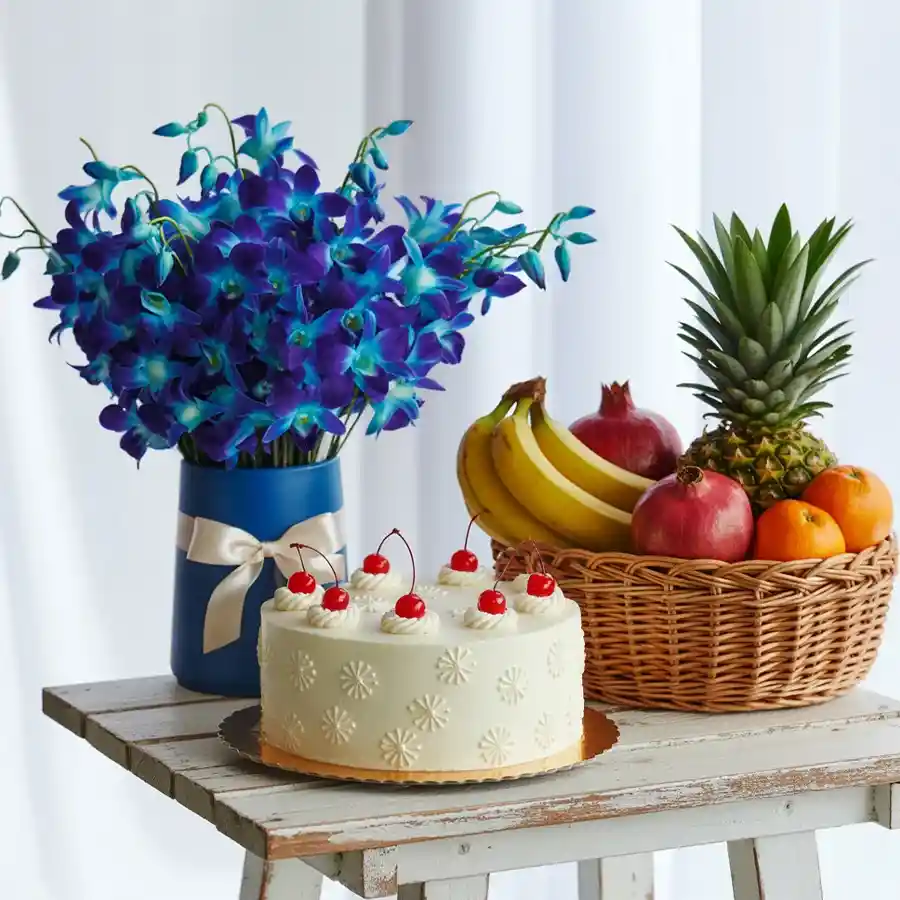 A delightful gift set featuring a butterscotch cake, blue orchids in a vase, a mixed fruit basket, and a bottle of fruit juice.