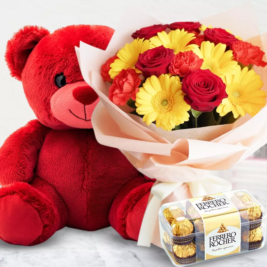 A colorful mixed floral bouquet with red roses, yellow gerberas, and red carnations, accompanied by a red teddy and Ferrero Rocher chocolates.