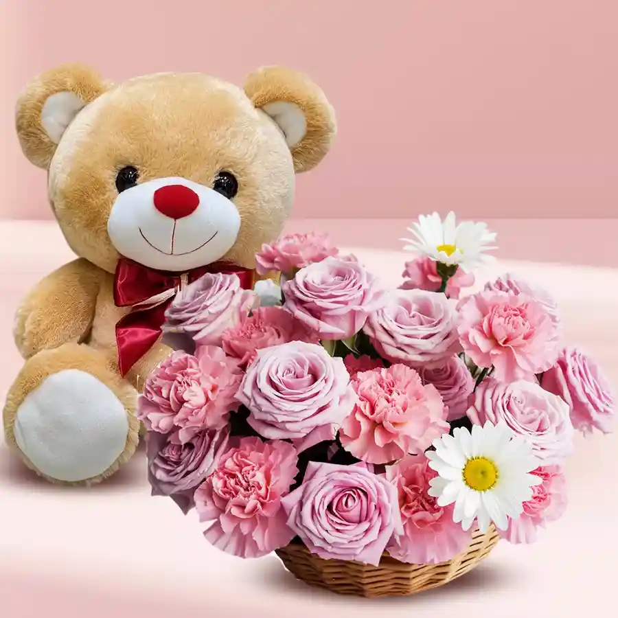 A charming basket filled with pink roses, pink carnations, daisies, and a soft cream teddy bear.
