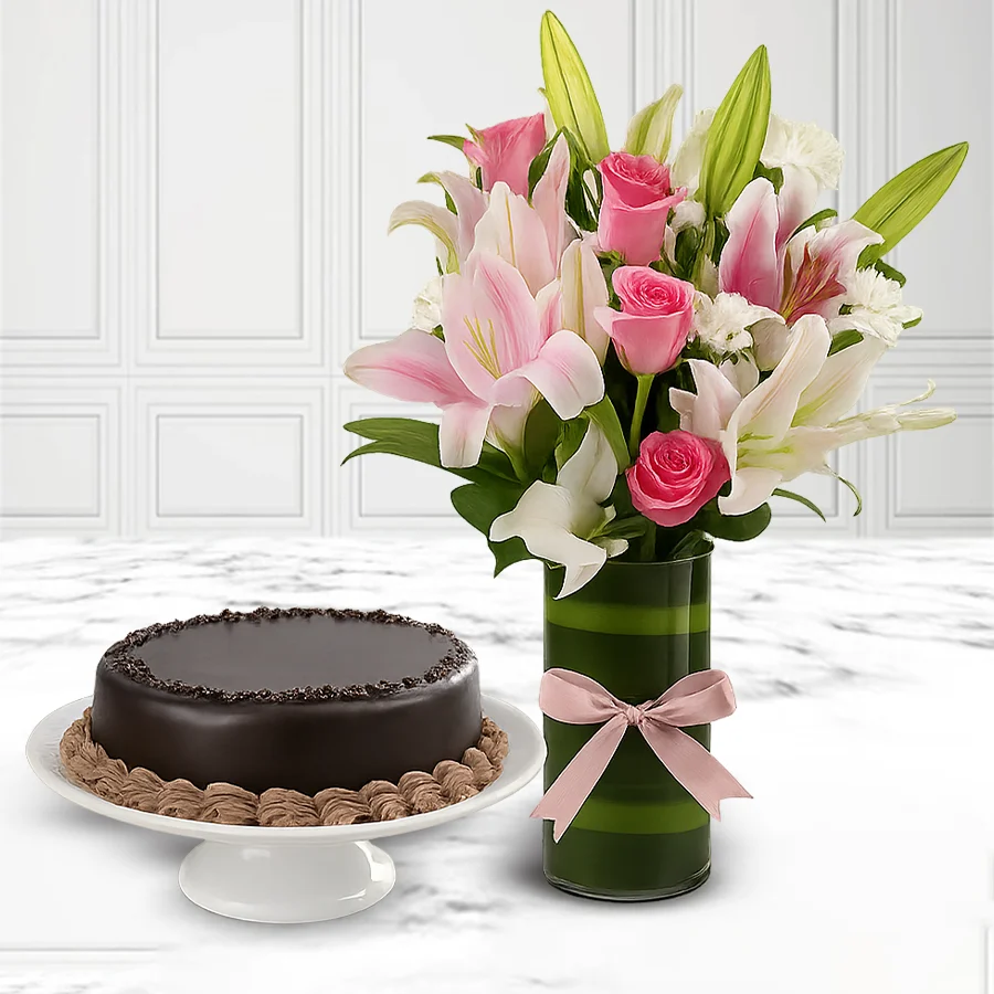 A stunning arrangement of flowers including white carnations and pink roses next to a 1 lb chocolate cake in a glass vase.
