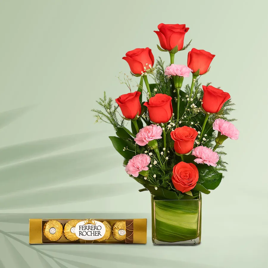 A stunning gift set featuring orange roses, pink carnations, and Ferrero Rocher chocolates arranged in a stylish vase.