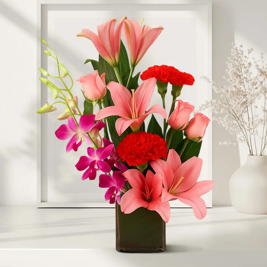 Mixed flowers arrangement featuring pink roses, red carnations, purple orchids, and pink Asiatic lilies in a clear glass vase.