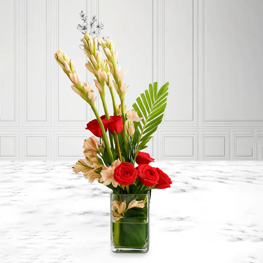 Beautiful arrangement of red roses and white rajnigandha in a glass vase.
