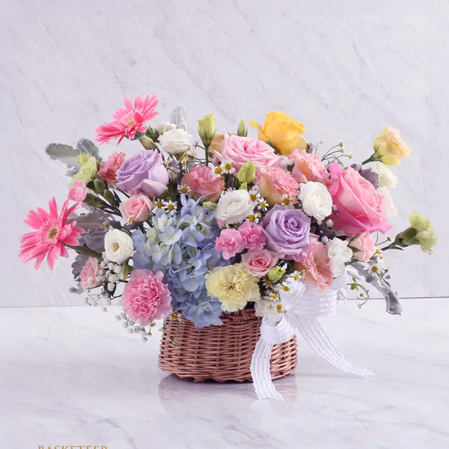 A colorful flower basket featuring yellow lilies, red carnations, yellow and white roses, and red gerberas in a vibrant arrangement.