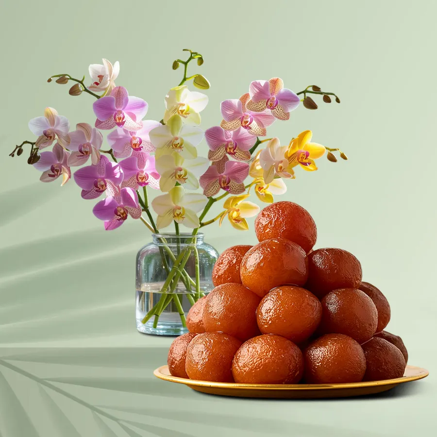 A stunning arrangement of mixed orchids in a glass vase alongside mini Gulab Jamoon sweets.