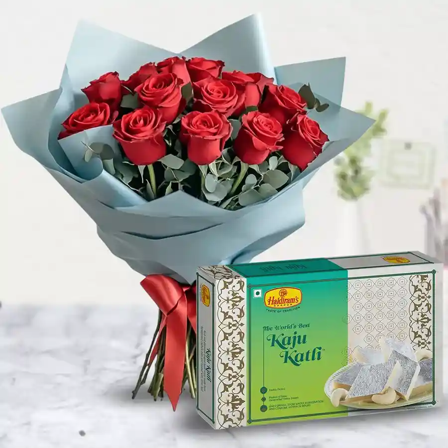 A beautiful arrangement of a dozen red roses alongside a box of Kaju Katli sweets, creating a delightful gift combination.