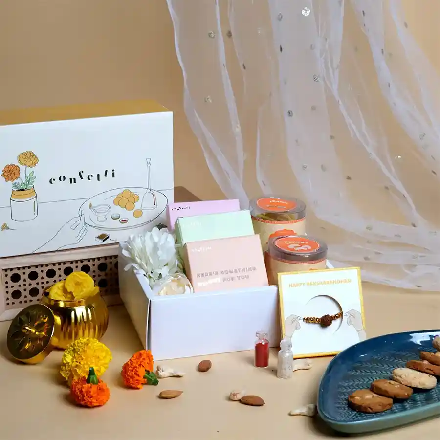 Festive Rakhi Snacks Gift Box featuring nuts, handmade cookies, a Rudraksha Rakhi, and an artificial flower in a yellow slider box.