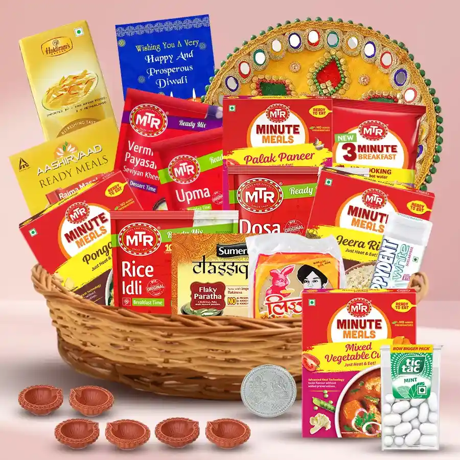 Tasty Diwali Celebration and Dinner Gifts Basket filled with ready-to-eat meals, savory snacks, sweet treats, a puja thali, diyas, and a silver-plated Ganesh-Lakshmi coin, all arranged in a reusable cane basket with a Diwali card.