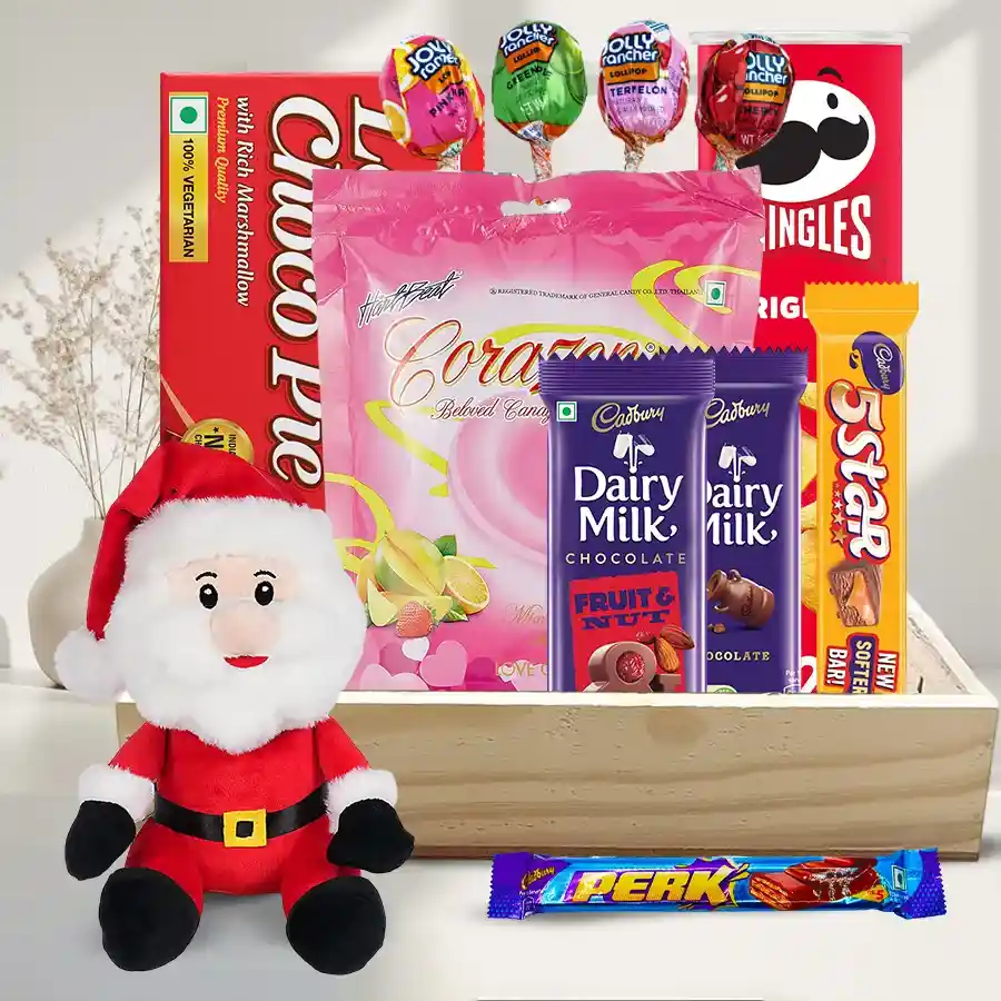 A festive gift hamper filled with Pringle Chips, Chocopie Family Pack, various Cadbury chocolates, Jolly Rancher lollipops, fruit pudding, a 9-inch Santa soft toy, and displayed on a stylish wooden tray.