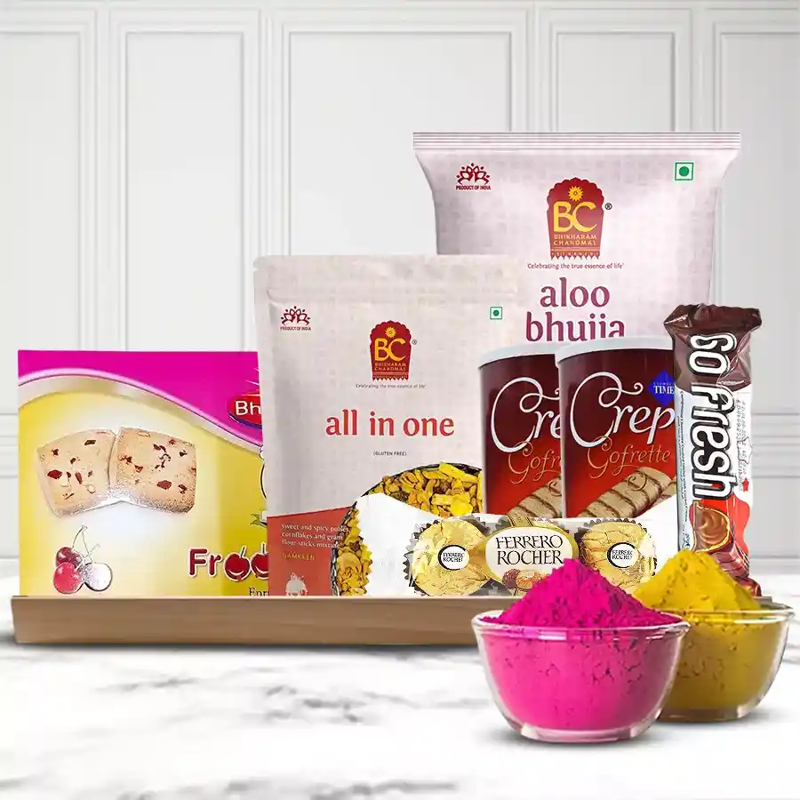 A decorative tray filled with a colorful assortment of sweets and snacks for Holi, including Bhikaram Froot Bites, Chanachur, Cizneci Time Crepe Choco Bars, Ferrero Rocher Chocolates, Go Fresh Choco Bar, and Bhikaram Alu Bhujia, topped with a pack of vibrant herbal Gulal.