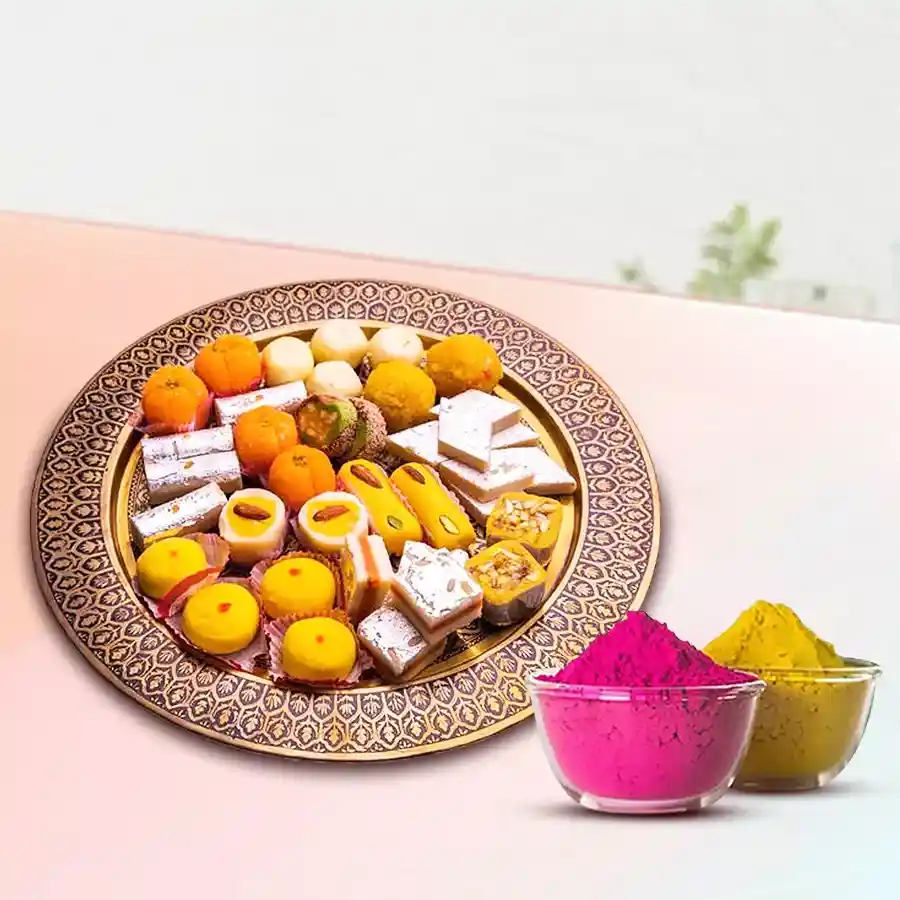 A beautifully arranged assortment of Indian sweets including Kaju Barfi, Kesar Peda, Desi Ghee Laddoos, and Mawa Gilori, presented in an elegant box, accompanied by two packets of organic herbal Gulal.