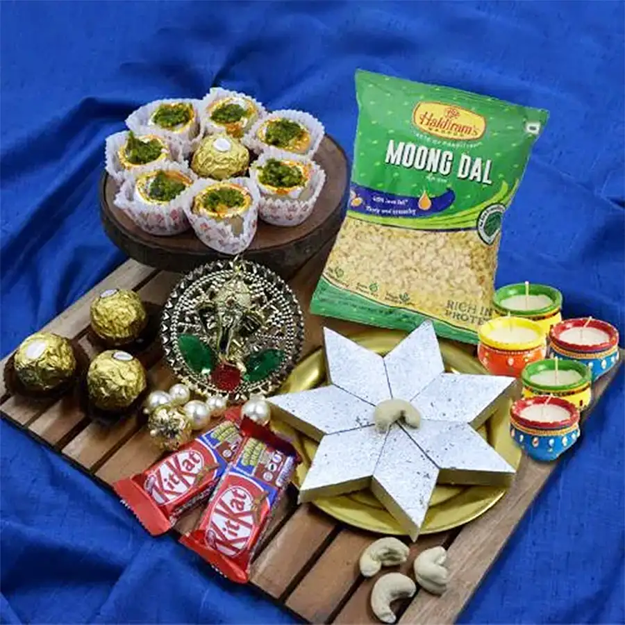 Distinctive Diwali Essentials Gift Combo featuring a golden puja thali, Ganesh Subh Labh decorations, Haldiram’s Kaju Katli, Kaju Pista sweets, Moong Dal, Ferrero Rocher, Nestle KitKat chocolates, and matka wax diyas.