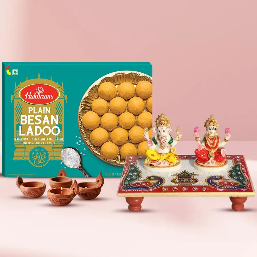 Divine Blessings Laxmi Ganesha Idol on a peacock-colored marble chowki with terracotta diyas and Haldiram besan laddus arranged on a festive background.