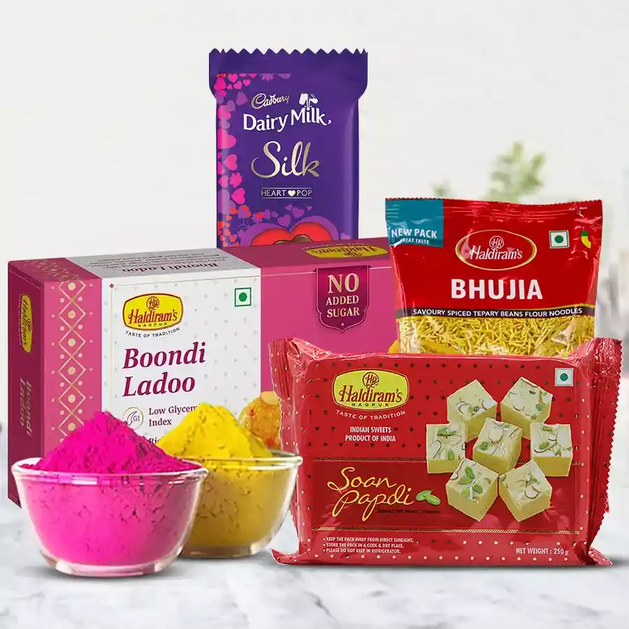 Gift bundle featuring Haldiram treats like Boondi Ladoo, Soan Papdi, and Bhujia, alongside a Cadbury Silk Heart Pop Out and colorful Herbal Gulal packets for Holi celebrations.