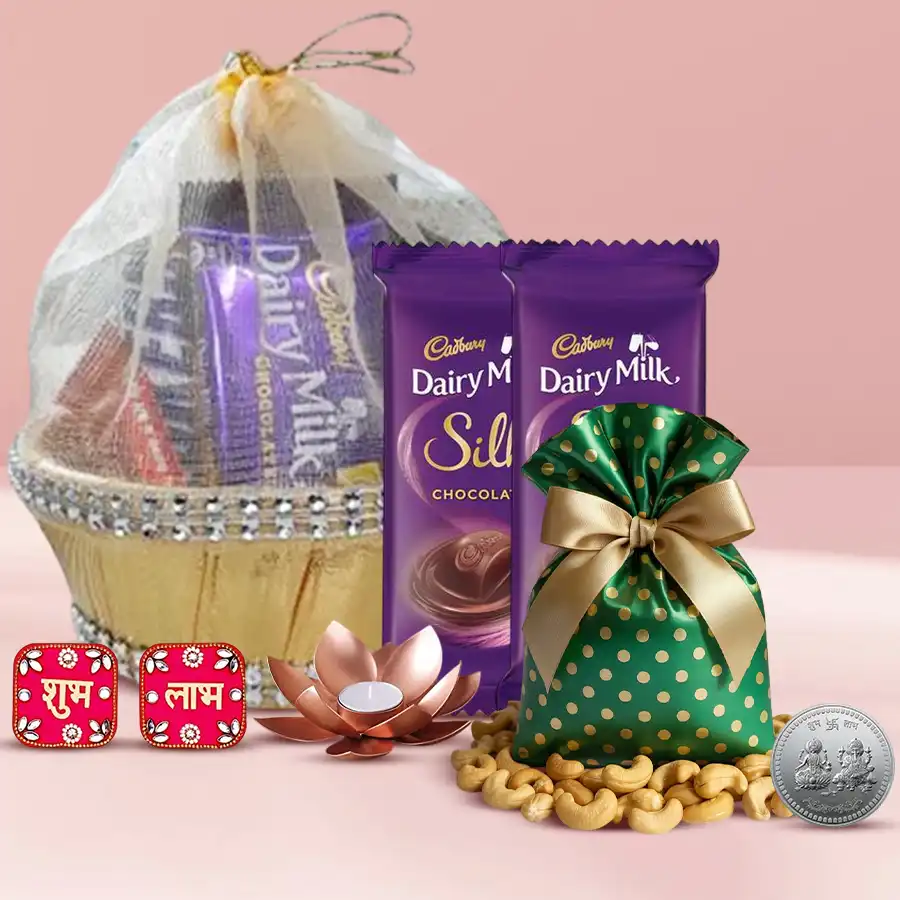 A decorative basket containing a 100g potli of cashews, two Cadbury Silk chocolate bars, a lotus tea light candle holder, a Shubh Labh wall sticker, and a silver-plated Ganesh Laxmi coin, all arranged for Diwali celebration.