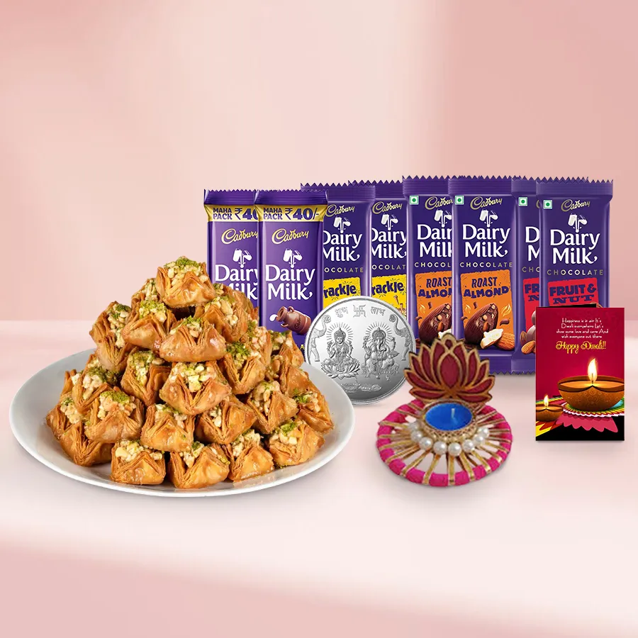 Gift basket featuring Pyramid Baklava, assorted Cadbury chocolates, silver-plated Ganesh Laxmi coin, Lotus Tea Light Candle Holder, and a personalized Diwali card arranged beautifully for Diwali celebration.