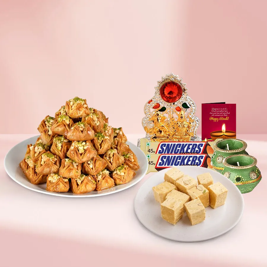 Pyramid Baklava Happy Pack with Soan Papdi, Snickers Almond bars, decorative wax diyas, and a Ganesh Laxmi Mandap arranged in a festive basket