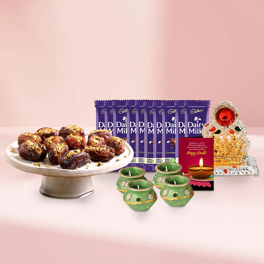 A decorative basket filled with Supreme Dates Baklava, Cadbury Dairy Milk bars, decorated wax diyas, and a Ganesh Laxmi Mandap, topped with a Diwali card.
