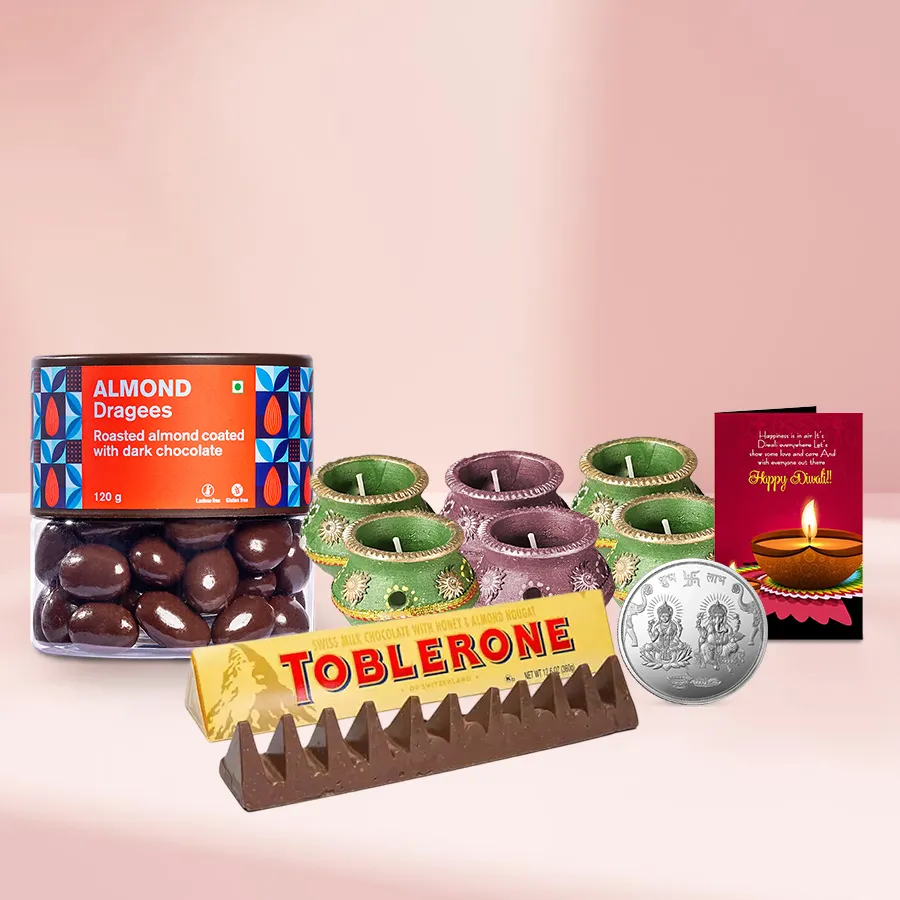 Chocolates N Enticing Almond Dragee gift basket featuring Almond Dragees, a Toblerone bar, wax diyas, a silver-plated Ganesh Laxmi coin, and a Diwali card.