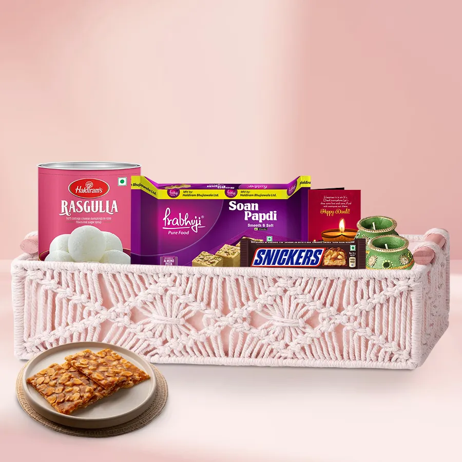 Diwali gift basket featuring Haldiram Rasgulla, Soan Papdi, Snickers bar, Peanut Chikkis, wax diyas, and a Diwali card, all beautifully arranged in a decorated basket.